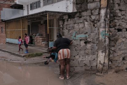 Priscila s'accroche à un mur criblé de balles tout en aidant une de ses filles à sauter par-dessus une flaque d'eau.