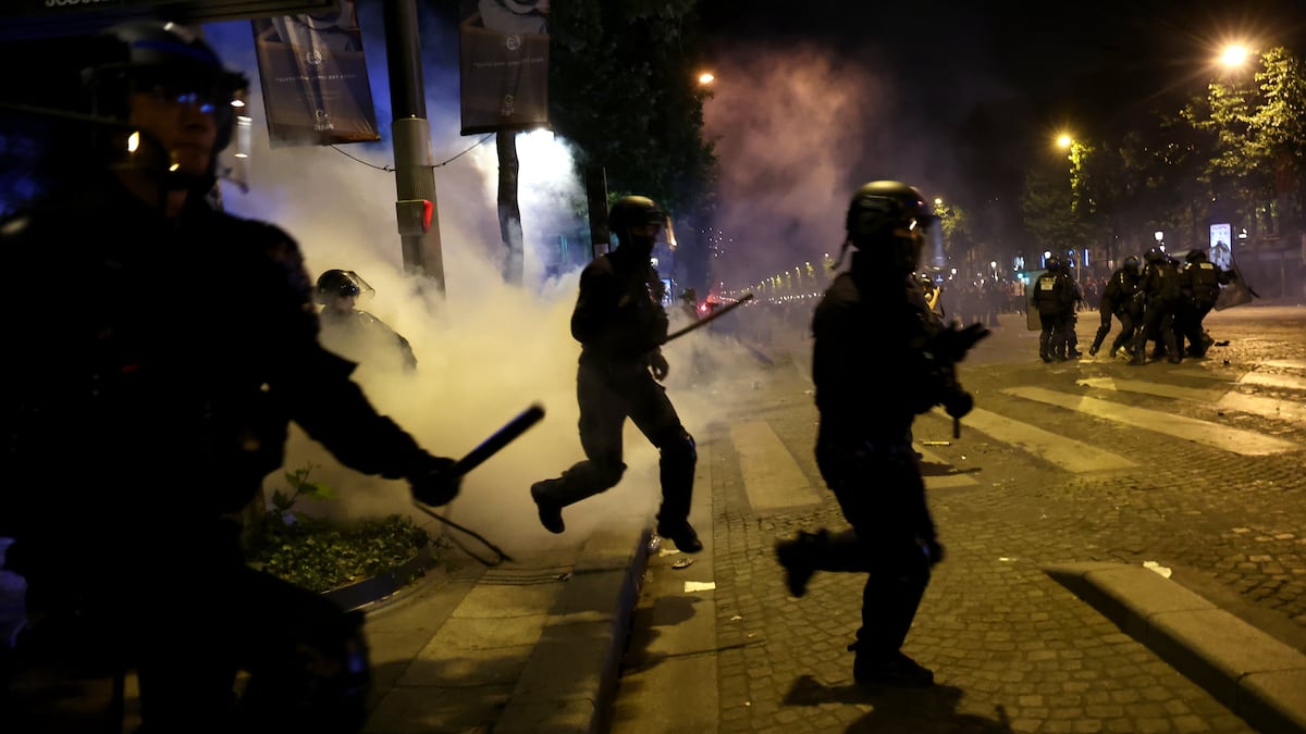 Agentes antidisturbios se protegen del lanzamiento de una bengala en los Campos Elíseos de París, este domingo.