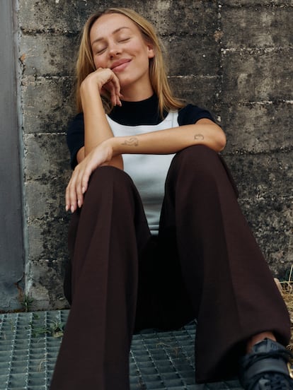 Ester Expósito transporte un dessus tricoté de cou licou blanc, un haut couché avec du cou haut, des pincettes et des chaussures avec boucle dorée, tous de Miu Miu.