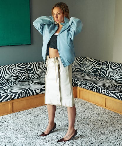 Veste de motard bleu transparent, jupe en cuir courte gris courte et structurée avec cravates et talon en cuir, tous de Prada.